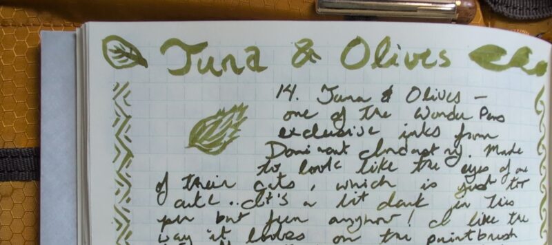 The top of a page of writing using the Tuna & Olives ink. The big lettering and doodles are done with a paintbrush and the rest is with the sailor fude dip pen I use for my swatches. The ink is consistently olive green, shading brighter into a more leafy green on the paintbrush. It shows some shading in the writing as well.