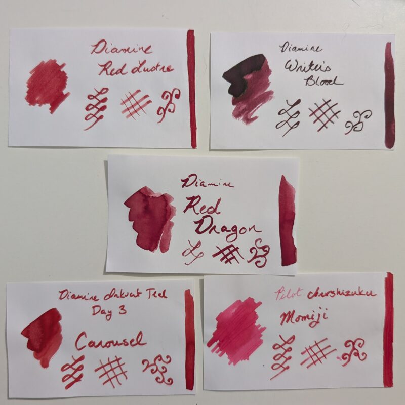 A set of fountain pen ink swatches photographed together for comparison. On the top row is Diamine Red Lustre and Diamine Writer's blood. In the centre is Diamine Red Dragon. At the bottom is Diamine Carousel and Pilot Iroshizuku Momiji.