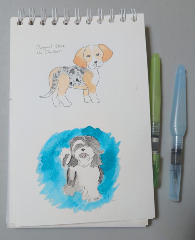 A notebook with two dogs painted in watercolour. The top one is labeled "Doggust 2026 Dunker" and features a beagle-like dog with a striking grey dappled pattern on middle and tail that contrasts with the tan and white on the rest of the dog. The one below that is not labelled but features a white and black Tibetan Terrier with long sweeping hair, and the area around the dog is coloured in a bright blue-teal using the Brilliant Mint fountain pen ink.