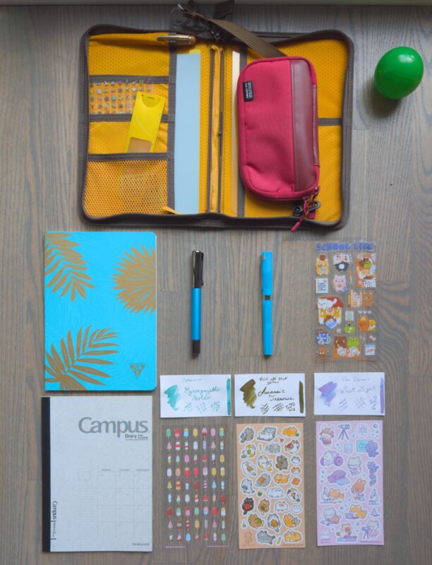 September 2026 setup including my usual a5 notebook cover and pencil case, a new clairfontaine notebook with monstera leaves on it, two pens, some stickers and ink (all named in the post)